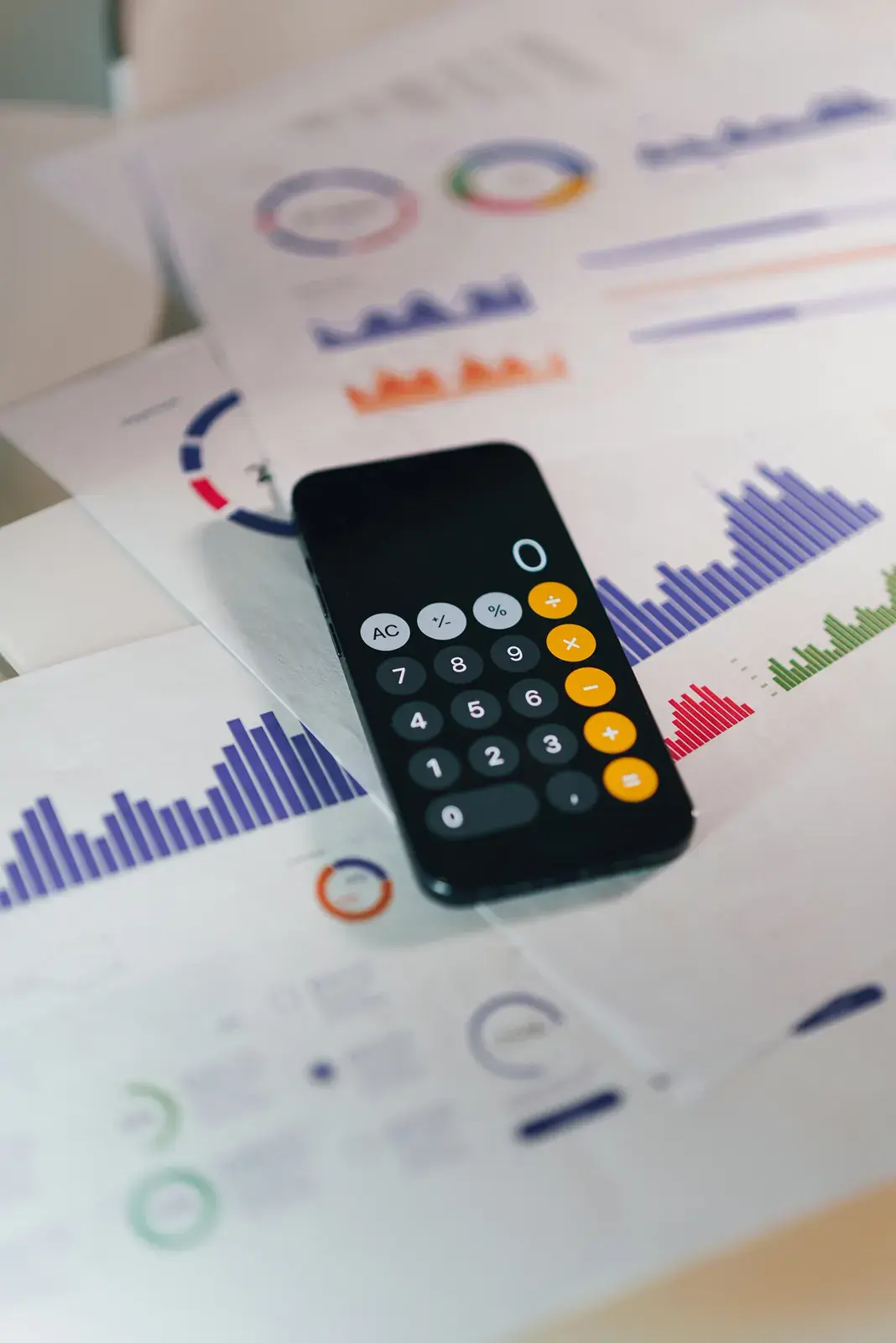 A phone calculator resting on printed financial charts and reports
