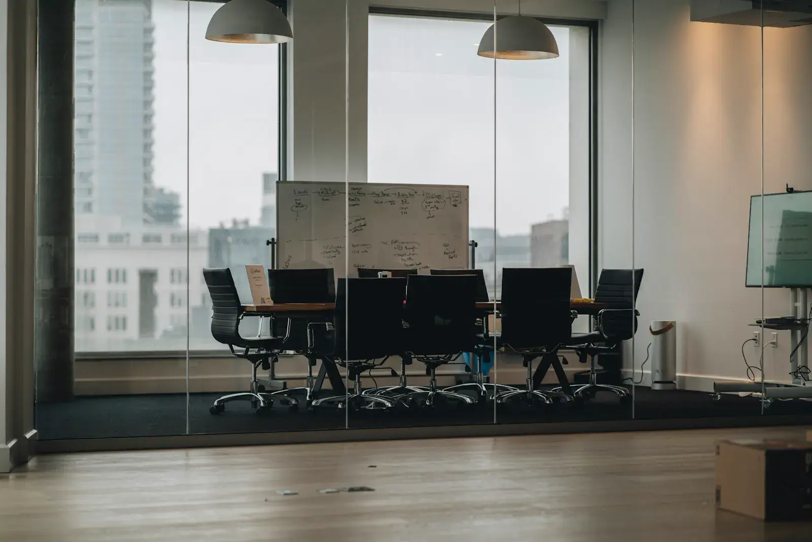 An empty glass-walled meeting room with a whiteboard and a view of city buildings