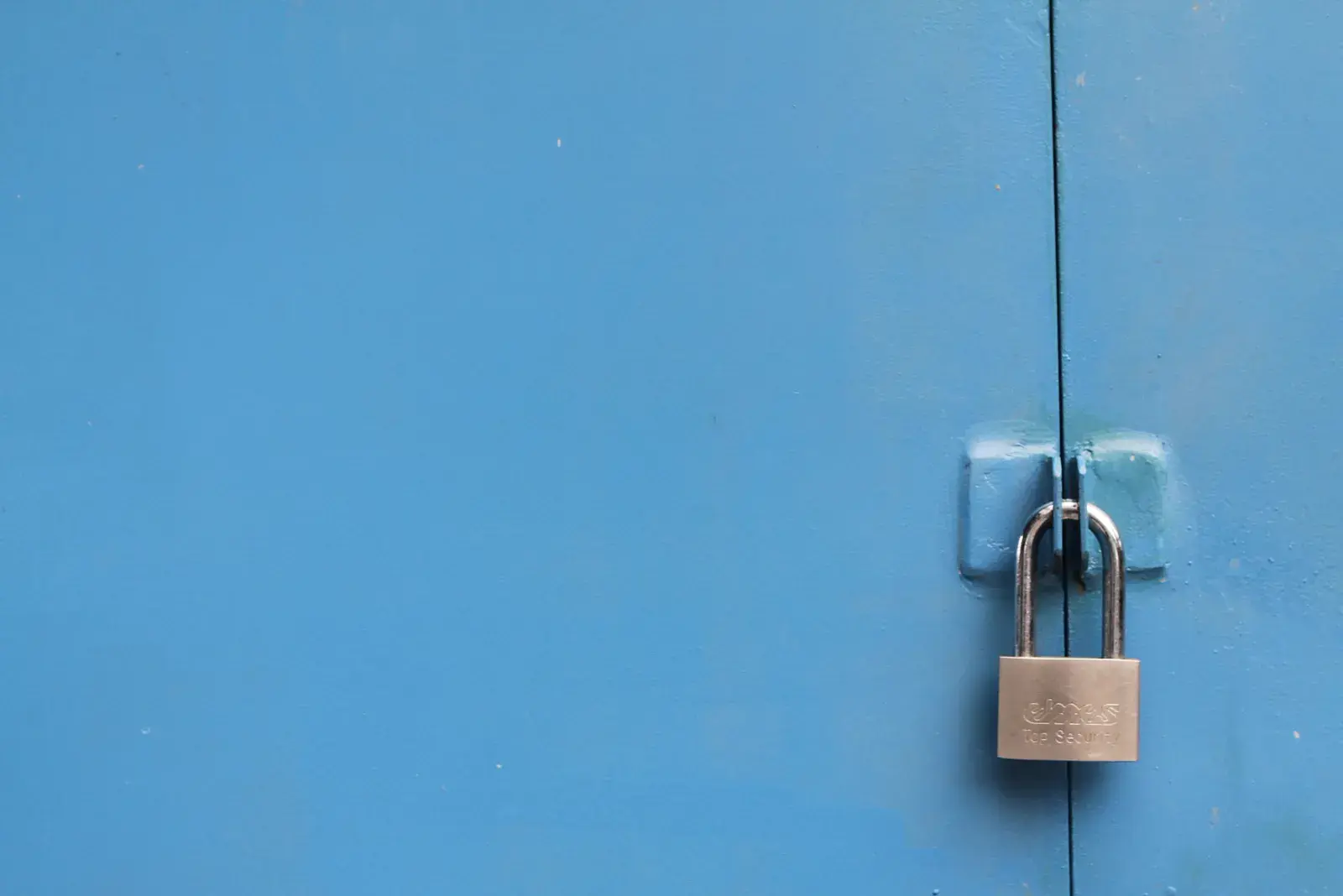 A steel padlock securing a blue metal door