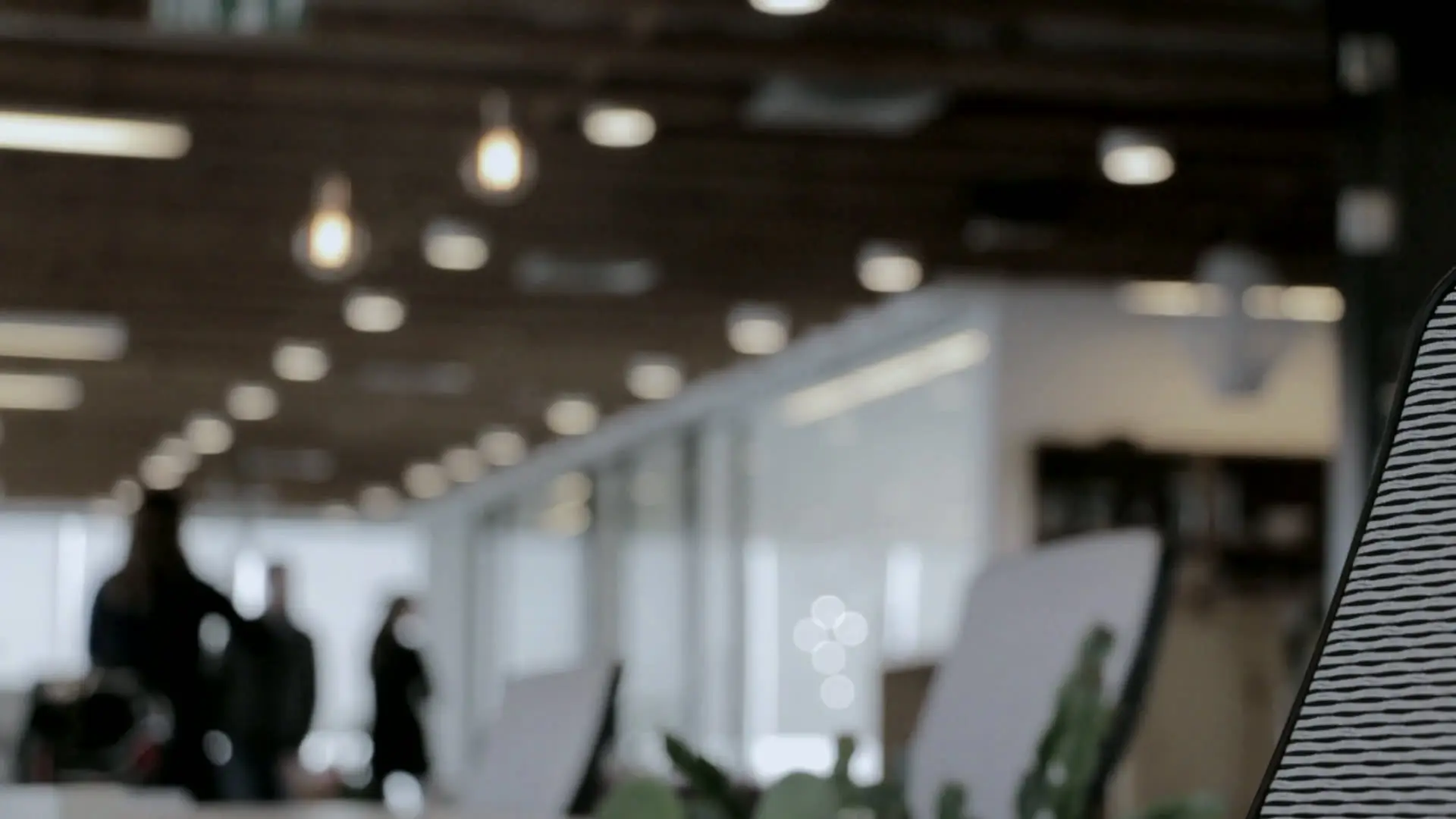 A busy open-plan office, softly out of focus, with people walking between desks