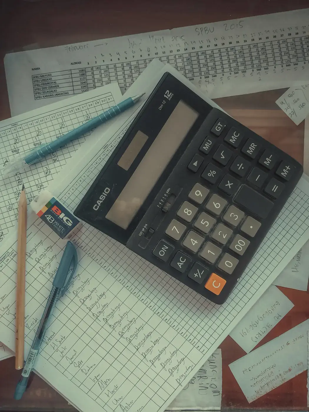 A desk calculator on top of handwritten ledger sheets and schedules