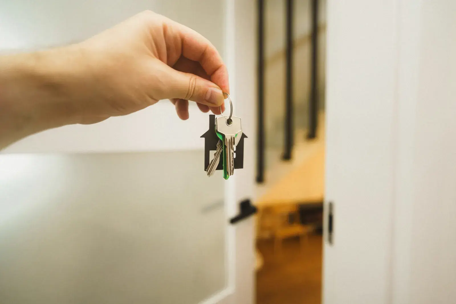A hand holding house keys on a house-shaped keyring in a doorway