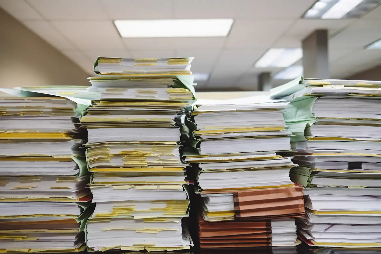 Tall stacks of tabbed client file folders piled on an office desk under fluorescent lights