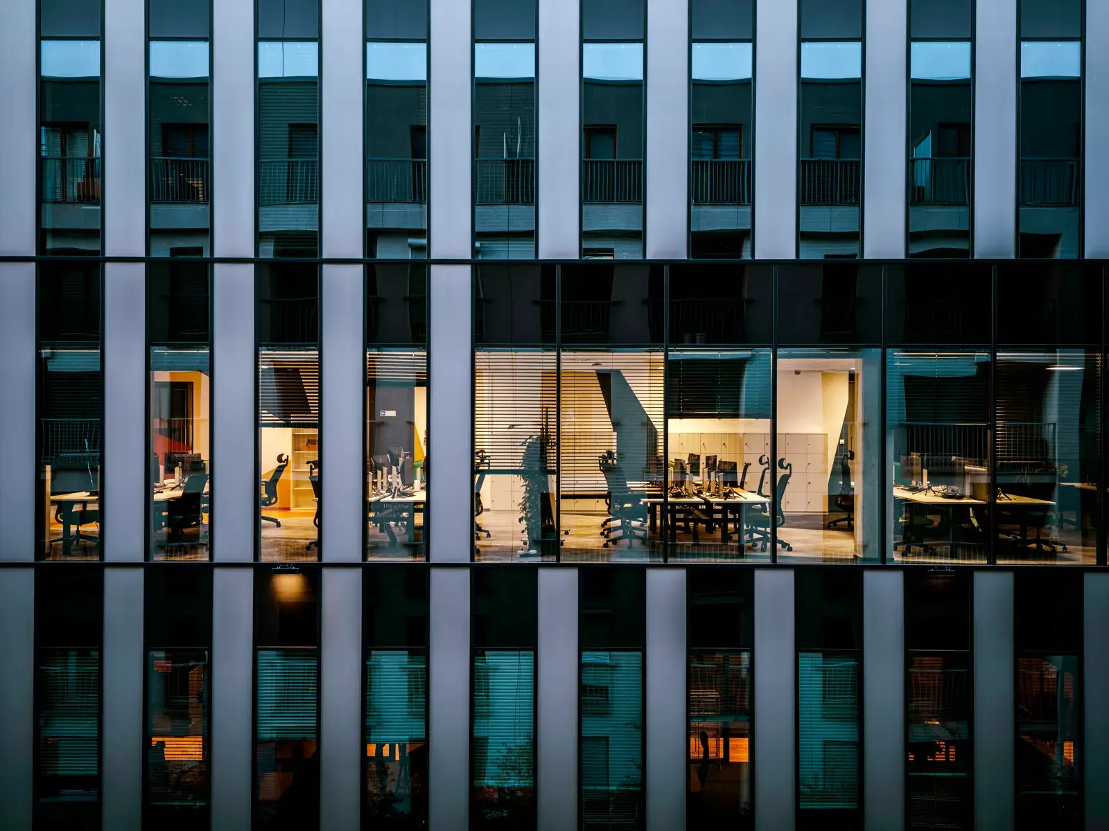An office building at dusk with one lit, empty office behind glass, everything shut down and in its place